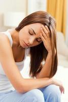 lijden van verschrikkelijk hoofdpijn. depressief jong vrouw zittend Aan bed en aanraken hoofd met hand- foto