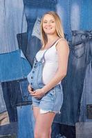 denim voor zwanger Dames. kant visie van mooi zwanger vrouw in jeans kleren Holding handen Aan haar buik terwijl staand tegen jeans achtergrond foto