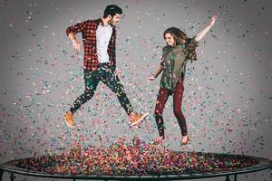 confetti plezier. in de lucht schot van mooi jong vrolijk paar jumping Aan trampoline samen met confetti allemaal in de omgeving van hen foto