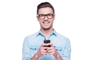 slim telefoon voor slim mensen knap jong Mens in overhemd op zoek Bij camera en Holding mobiel telefoon terwijl staand tegen wit achtergrond foto