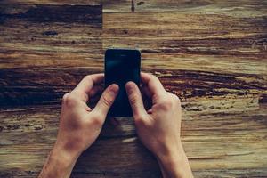 typen snel bericht. detailopname top visie van mannetje handen Holding mobiel telefoon over- de rustiek houten bureau foto