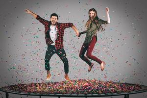 pret in beweging. in de lucht schot van mooi jong vrolijk paar Holding handen terwijl jumping Aan trampoline samen met confetti allemaal in de omgeving van hen foto