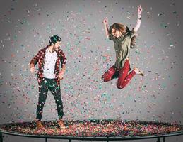 pret tijd samen. in de lucht schot van mooi jong vrolijk paar jumping Aan trampoline samen met confetti allemaal in de omgeving van hen foto