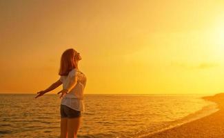 gelukkige jonge vrouw opent haar armen naar de hemel bij zonsondergang