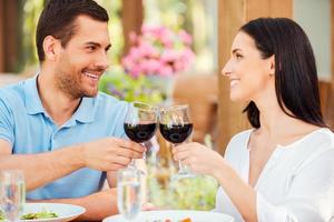 romantisch datum in restaurant. gelukkig jong liefhebbend paar roosteren met rood wijn en glimlachen terwijl ontspannende in buitenshuis restaurant samen foto