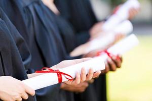 afgestudeerden met diploma's. detailopname van vier college afgestudeerden staand in een rij en Holding hun diploma's