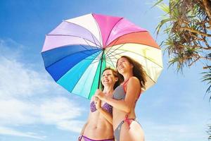 zusters met regenboogparaplu op het strand
