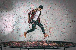 in de lucht plezier. in de lucht schot van knap jong Mens jumping Aan trampoline met confetti allemaal in de omgeving van hem foto