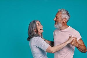 mooi senior paar dansen en glimlachen terwijl staand samen tegen blauw achtergrond foto