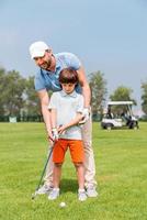 vader is altijd in de buurt naar helpen mij. blij jong manteaching zijn zoon naar Speel golf terwijl staand Aan de golf Cursus foto