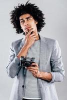 wat zal ik schieten De volgende knap jong Afrikaanse Mens Holding retro gestileerd camera en op zoek attent terwijl staand tegen grijs achtergrond foto