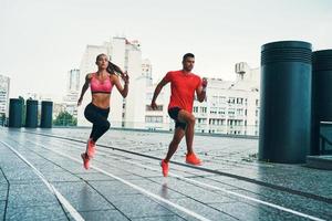 vol lengte van twee jong mensen in sport- kleding jumping en jogging terwijl oefenen Aan de stad straat buitenshuis foto