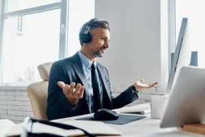 zelfverzekerd zakenman in hoofdtelefoons gebaren terwijl hebben web conferentie in de kantoor foto