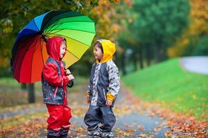 twee schattige kinderen, jongensbroers, spelen in park met paraplu foto