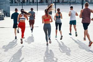 vol lengte achterzijde visie van mensen in sport- kleding jogging terwijl oefenen Aan de trottoir buitenshuis foto