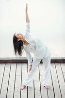 uitrekken naar de zon. vol lengte van mooi jong vrouw in wit kleding het uitvoeren van yoga buitenshuis foto