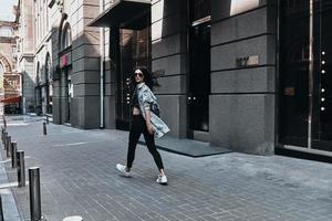 stad meisje. vol lengte achterzijde visie van jong vrouw op zoek over- haar schouder terwijl wandelen naar beneden de straat foto