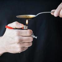 Mens koken heroïne. detailopname van Mens koken heroïne in lepel terwijl Holding een injectiespuit in zijn hand- foto