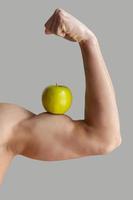 gezond levensstijl. bijgesneden beeld van gespierd Mens tonen zijn perfect biceps met een groen appel Aan het terwijl geïsoleerd Aan grijs achtergrond foto