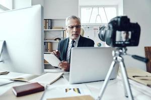 senior Mens in elegant bedrijf pak gebruik makend van modern technologieën terwijl maken sociaal media video foto