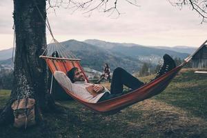 mooi hoor avond. knap jong Mens aan het liegen in hangmat en glimlachen terwijl camping met zijn vriendin foto