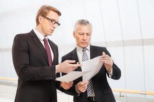 bedrijf discussie. twee zelfverzekerd bedrijf mannen bespreken iets terwijl Holding papieren in hun handen foto