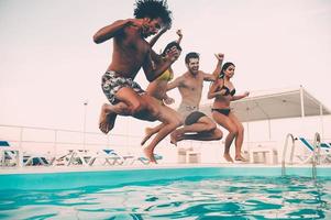 zomer zwembad feest. groep van mooi jong mensen op zoek gelukkig terwijl jumping in de zwemmen zwembad samen foto