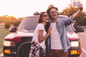 vastleggen plezier. mooi jong paar bonding naar elk andere en leunend Bij hun oppakken vrachtauto terwijl maken selfie foto