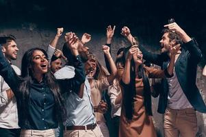 genieten van verbazingwekkend feest. groep van mooi jong mensen dansen met Champagne fluiten en op zoek gelukkig foto