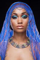 fascinerend schoonheid. mooi Afrikaanse vrouw aan het bedekken hoofd door sjaal en op zoek Bij camera terwijl staand tegen zwart achtergrond foto