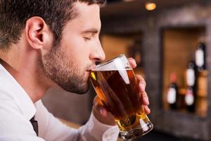 Mens drinken bier. kant visie van knap jong Mens drinken bier terwijl zittend Bij de bar teller foto