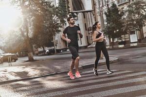 vol van energie. vol lengte van jong paar in sport kleding rennen door de stad straat samen foto