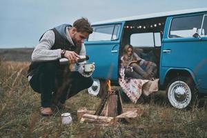 genieten van mooi hoor dag. mooi jong vrouw lezing een boek terwijl haar vriendje gieten een drinken door de vreugdevuur foto