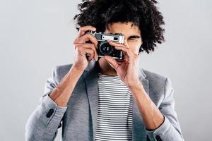 focus Aan u knap jong Afrikaanse Mens Holding retro gestileerd camera en scherpstellen Aan u terwijl staand tegen grijs achtergrond foto