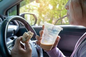 Aziatisch dame Holding ijs koffie en brood bakkerij voedsel in auto gevaarlijk en risico een ongeluk. foto