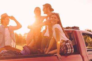 genieten van weg reis met vrienden. groep van jong vrolijk mensen genieten van hun weg reis terwijl zittend in oppakken vrachtauto samen foto