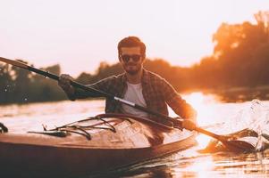 kajakken is mijn leven jong glimlachen Mens kajakken Aan rivier- met zonsondergang in de achtergrond foto