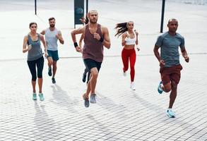 vol lengte van mensen in sport- kleding jogging terwijl oefenen Aan de trottoir buitenshuis foto