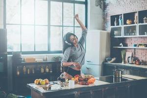 Koken met passie. mooi jong gemengd ras vrouw in hoofdtelefoons Koken salade en dansen terwijl staand in keuken Bij huis foto