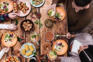 genieten van Super goed diner. top visie van vier mensen hebben avondeten samen terwijl zittend Bij de rustiek houten tafel foto