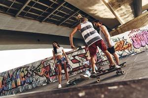 zorgeloos tijd met vrienden. vol lengte van jong modern mensen met skates hangende uit samen buitenshuis foto