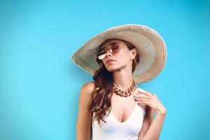 portret van mooi jong vrouw in elegant hoed op zoek weg terwijl staand tegen blauw achtergrond foto