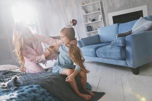 mooi jong moeder op zoek Bij haar schattig dochter en glimlachen terwijl zittend Aan de bed Bij huis foto