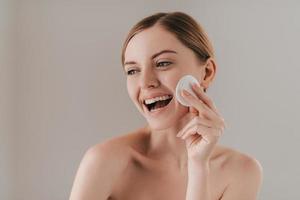 brengen versheid naar haar huid. studio portret van aantrekkelijk vrouw reiniging haar huid met een katoen stootkussen terwijl staand tegen achtergrond foto