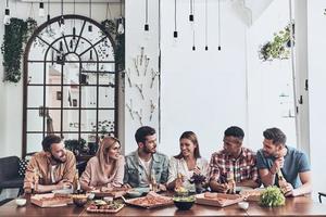 vrienden maken elk andere gelukkig. mooi jong mensen in gewoontjes slijtage pratend en glimlachen terwijl hebben een avondeten partij in de restaurant foto