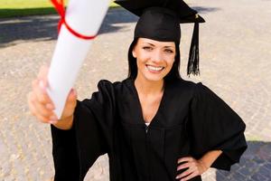 gelukkig afstuderen met diploma. top visie van gelukkig jong vrouw in diploma uitreiking japon tonen haar diploma en glimlachen