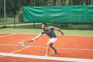 spelen tennis. zelfverzekerd jong Mens in sport- kleren spelen tennis Aan tennis rechtbank foto