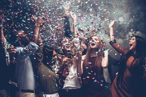 ontketend plezier. groep van mooi jong mensen het werpen kleurrijk confetti terwijl dansen en op zoek gelukkig foto