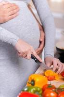 enkel en alleen gezond voedsel. gelukkig jong paar Koken samen in de keuken terwijl Mens aanraken buik van zijn zwanger vrouw foto