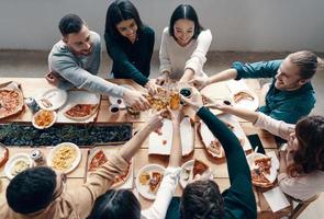 groep van jong mensen in gewoontjes slijtage plukken pizza en glimlachen terwijl hebben een avondeten partij binnenshuis foto